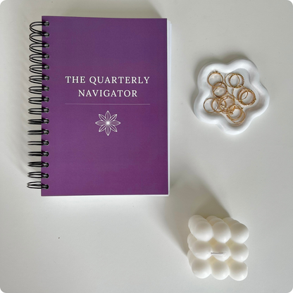 The Quarterly Navigator productivity planner by Agile Bloom — flat lay showing the cover design in purple with feminine desk accessories.